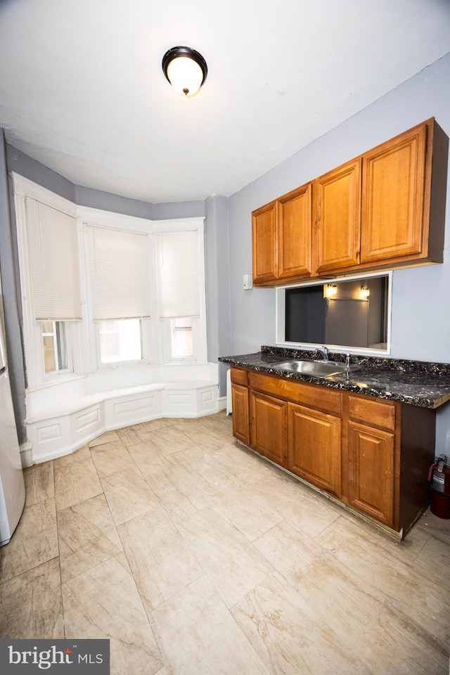 kitchen featuring dark stone countertops, brown cabinetry, and a sink