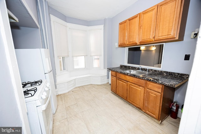 kitchen with dark stone countertops, white range with gas stovetop, brown cabinets, and a sink