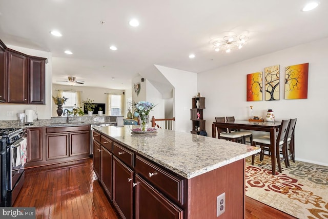 kitchen with stainless steel gas range oven, dark wood-type flooring, a sink, a center island, and light stone countertops