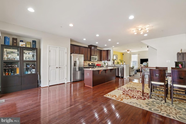 kitchen featuring a center island, open floor plan, appliances with stainless steel finishes, a kitchen breakfast bar, and dark wood-style flooring