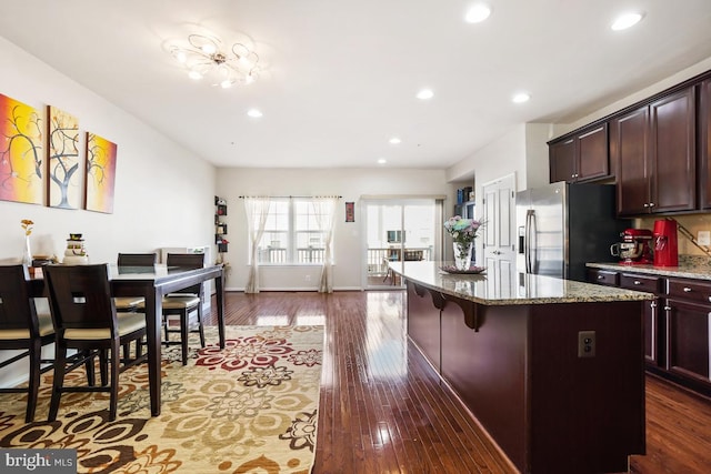 kitchen featuring light stone counters, stainless steel fridge, a center island, and dark wood-style flooring