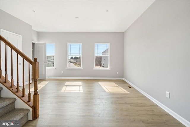 unfurnished living room featuring light wood finished floors, stairs, and baseboards