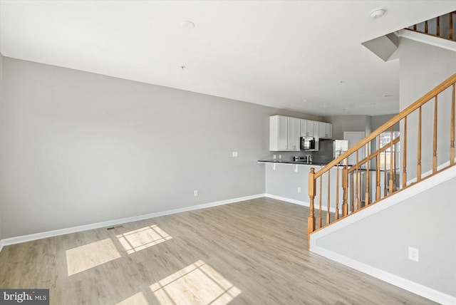 empty room with baseboards, light wood-style floors, and stairs