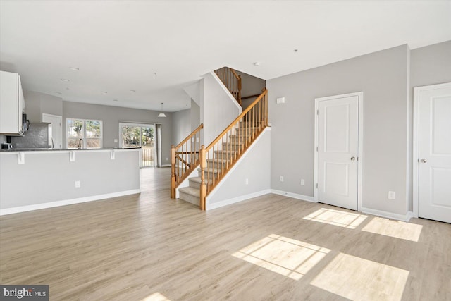 unfurnished living room with stairway, light wood-style floors, and baseboards