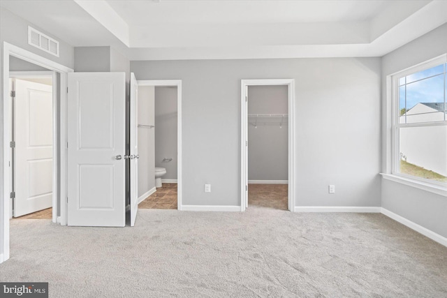 unfurnished bedroom featuring visible vents, baseboards, carpet, and a walk in closet