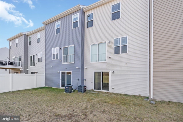 rear view of property with a lawn, central AC unit, and fence