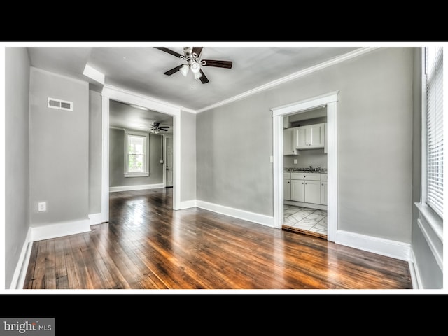 empty room with hardwood / wood-style floors, crown molding, baseboards, and visible vents