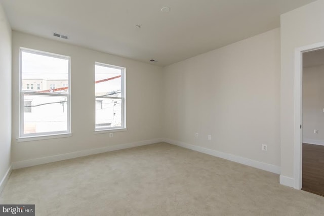 spare room featuring visible vents, light colored carpet, and baseboards