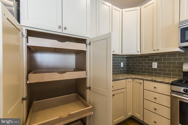 kitchen featuring decorative backsplash, white cabinets, stainless steel appliances, and dark stone counters