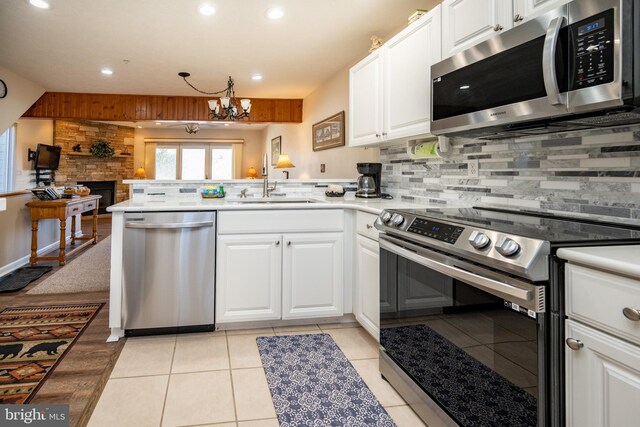 kitchen featuring tasteful backsplash, a peninsula, a notable chandelier, white cabinets, and stainless steel appliances