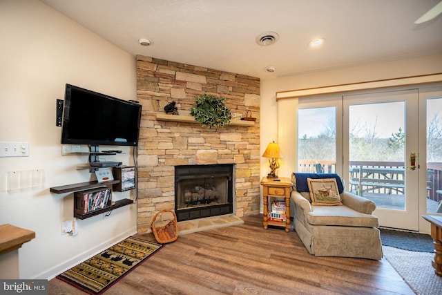 living area featuring a stone fireplace, baseboards, and wood finished floors