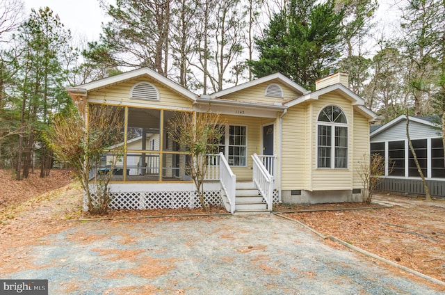 view of front of property featuring a porch, a chimney, a sunroom, and crawl space