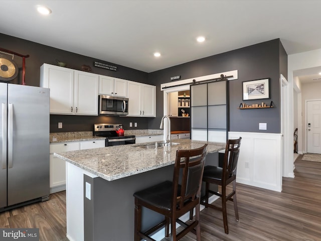 kitchen with a sink, wainscoting, stainless steel appliances, white cabinetry, and dark wood-style flooring