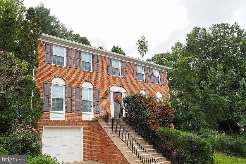 colonial-style house featuring a garage, brick siding, and stairway