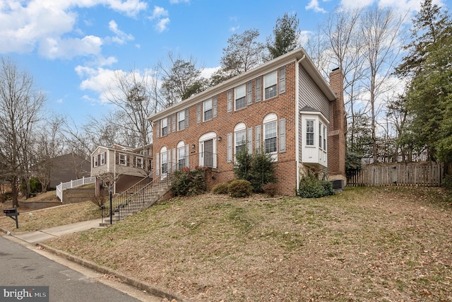 view of front of home with brick siding, a chimney, and fence