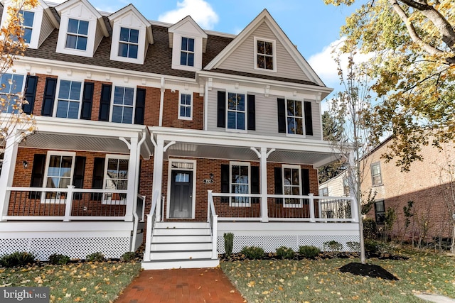 townhome / multi-family property with a porch, brick siding, roof with shingles, and a front lawn