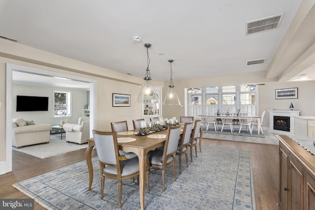 dining area with visible vents, a warm lit fireplace, and wood finished floors