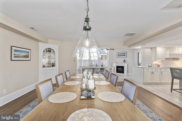 dining space featuring light wood-type flooring, visible vents, a warm lit fireplace, and ceiling fan