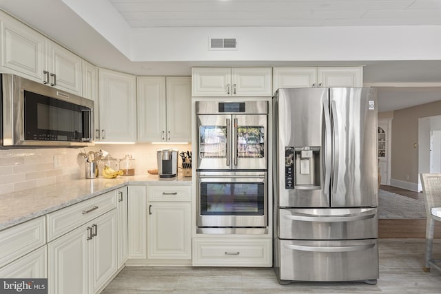 kitchen with light stone countertops, visible vents, stainless steel appliances, white cabinets, and tasteful backsplash