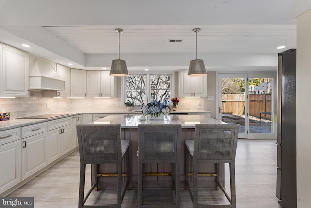 kitchen featuring visible vents, black electric stovetop, a breakfast bar area, custom range hood, and freestanding refrigerator