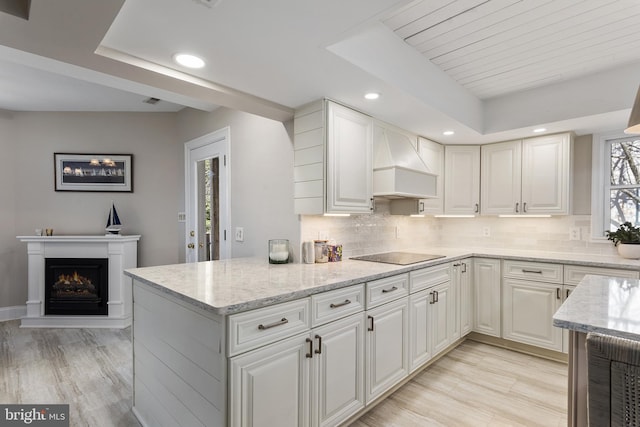 kitchen with premium range hood, black electric cooktop, tasteful backsplash, and a tray ceiling