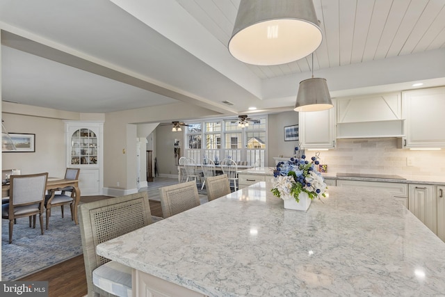 kitchen featuring light stone countertops, custom exhaust hood, ceiling fan, decorative backsplash, and black electric cooktop