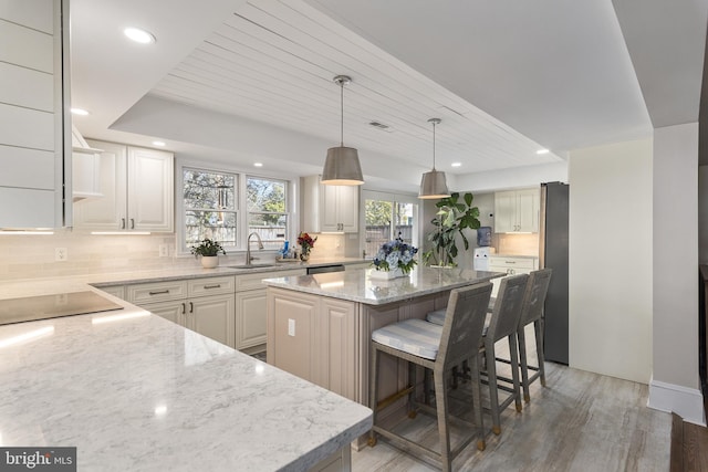 kitchen with a sink, backsplash, a center island, black electric cooktop, and light stone countertops