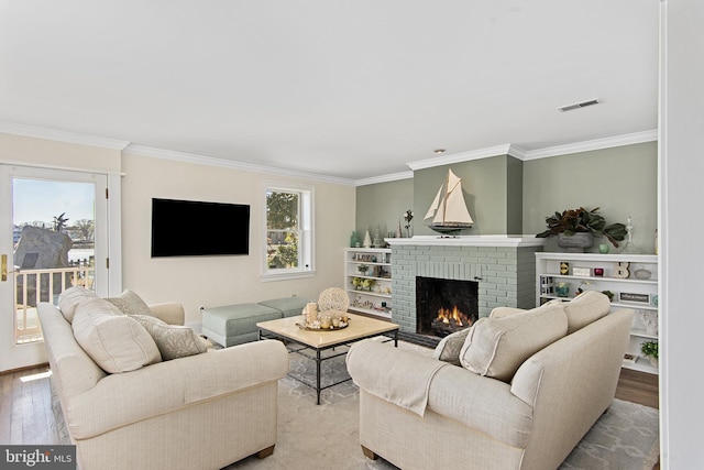 living room featuring a brick fireplace, wood finished floors, visible vents, and ornamental molding