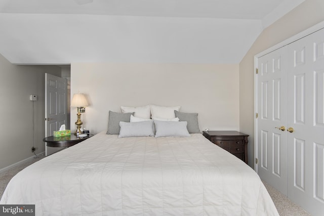 carpeted bedroom featuring a closet, lofted ceiling, and baseboards