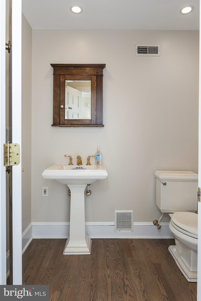 half bathroom with toilet, wood finished floors, visible vents, and baseboards