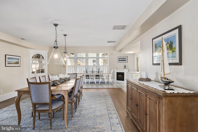 dining area with visible vents, baseboards, a warm lit fireplace, and dark wood-style floors