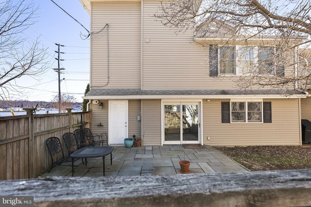 rear view of house with a patio, fence, and a shingled roof