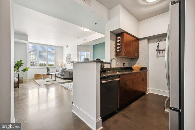 kitchen with a sink, finished concrete flooring, appliances with stainless steel finishes, decorative backsplash, and baseboards