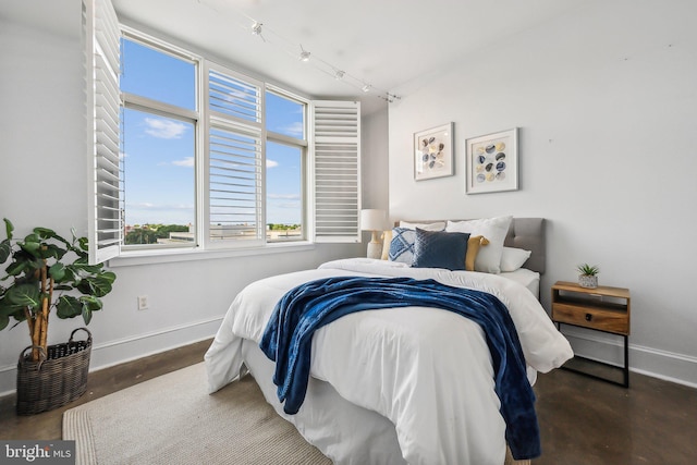 bedroom featuring baseboards, finished concrete flooring, and rail lighting