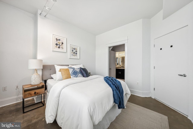 bedroom with baseboards, concrete flooring, and ensuite bath