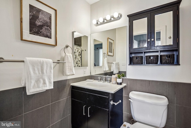 full bathroom featuring toilet, curtained shower, tile walls, wainscoting, and vanity