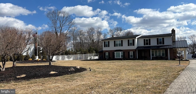 view of front facade with a front lawn, a standing seam roof, fence, metal roof, and brick siding