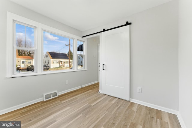 unfurnished room featuring a barn door, baseboards, visible vents, and wood finished floors