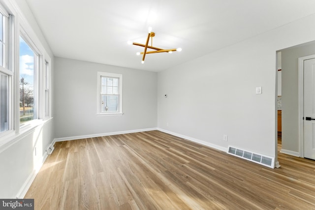 spare room featuring a notable chandelier, visible vents, light wood-style flooring, and baseboards