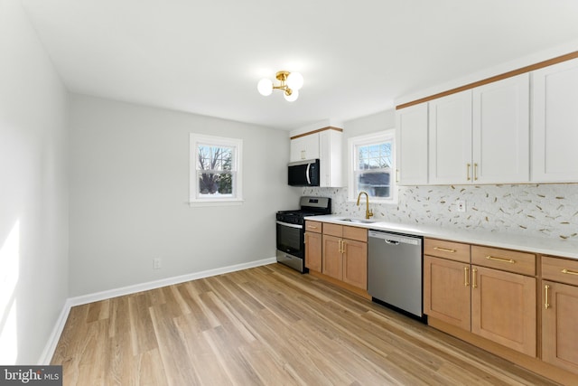 kitchen featuring light wood-style flooring, a sink, tasteful backsplash, stainless steel appliances, and light countertops