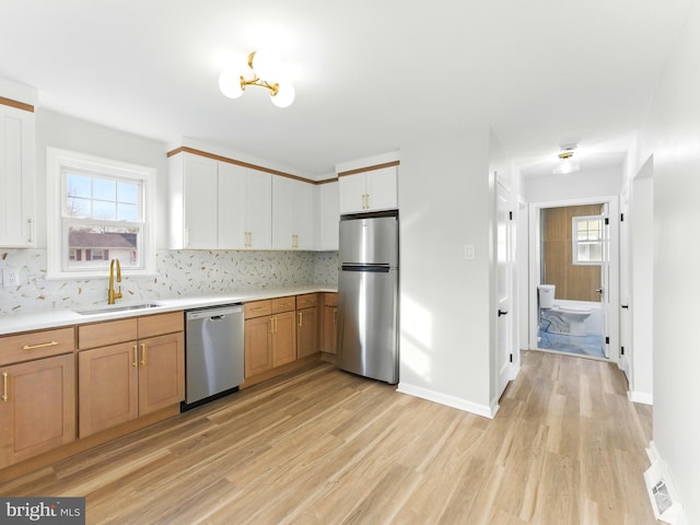 kitchen with light wood finished floors, backsplash, appliances with stainless steel finishes, and a sink