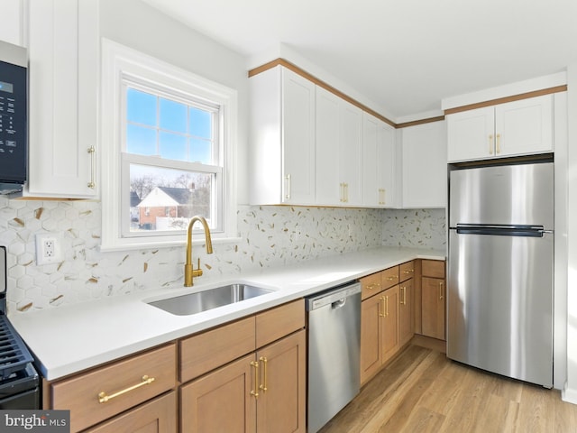 kitchen with light wood finished floors, tasteful backsplash, light countertops, appliances with stainless steel finishes, and a sink