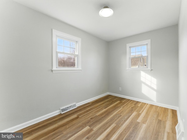 spare room featuring wood finished floors, visible vents, and baseboards