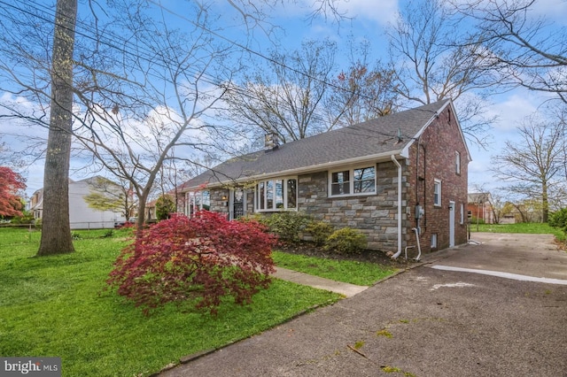 view of front of property featuring aphalt driveway, stone siding, roof with shingles, a front yard, and a chimney