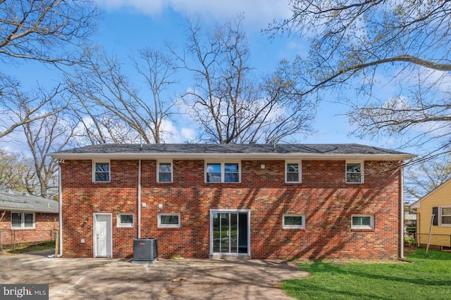 back of house with brick siding, a patio area, a lawn, and central AC