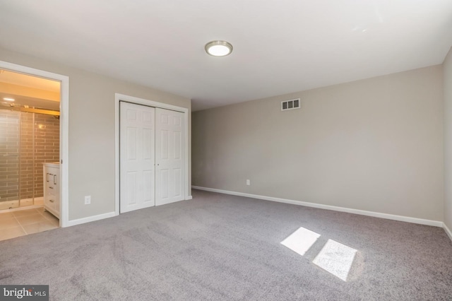 unfurnished bedroom featuring baseboards, visible vents, carpet floors, ensuite bath, and a closet