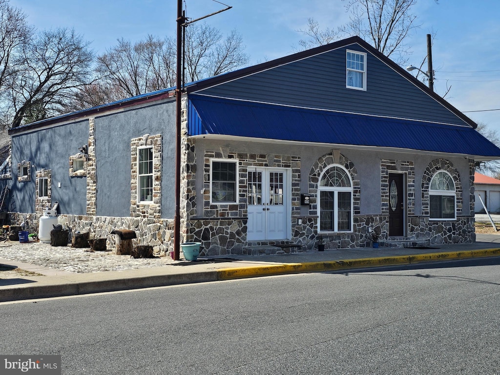 view of front of home with french doors, stone siding, metal roof, and stucco siding