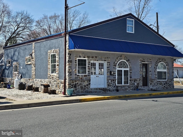 view of front of home with french doors, stone siding, metal roof, and stucco siding