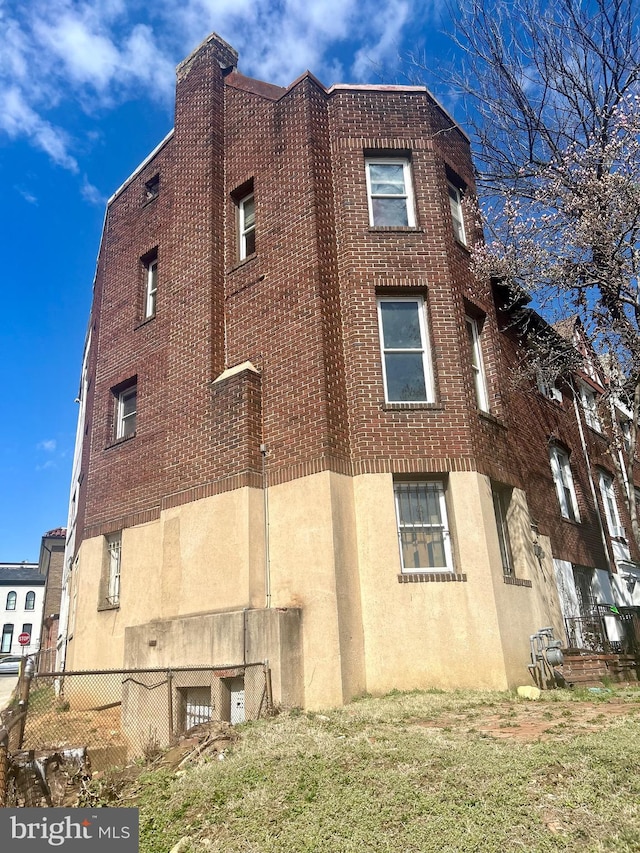 view of side of home with brick siding, stucco siding, and fence