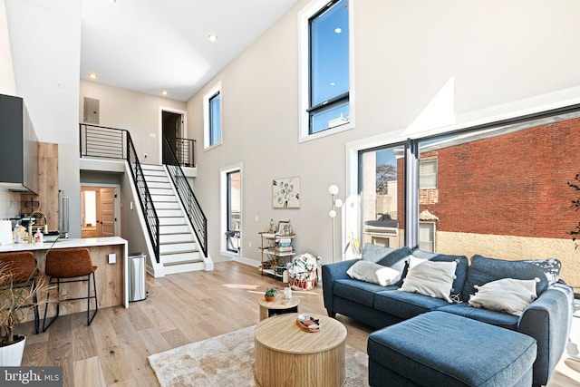 living area with baseboards, stairway, recessed lighting, light wood-style flooring, and a high ceiling